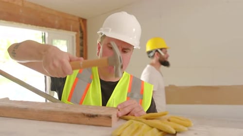 Man Hammering a Nail into Wood at Construction Site