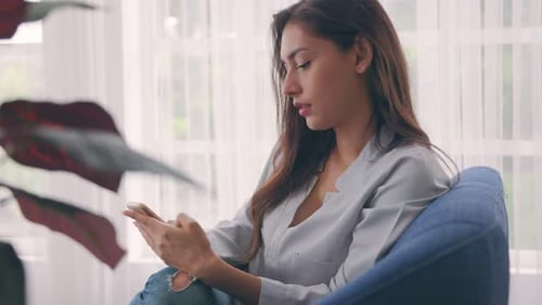 Woman Using Smartphone Relaxing on Chair at Home