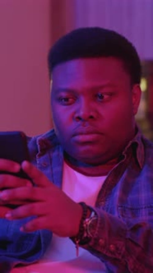 Portrait Focused Young African American Man Typing Message and Looking at Smartphone Screen Sitting
