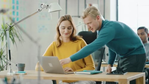 Coworkers Collaborate on Laptop in Modern Office