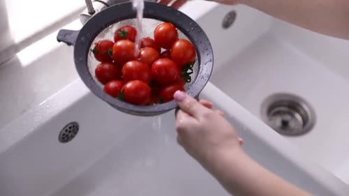 Woman washing cherry tomatoes in sieve at sink, closeup