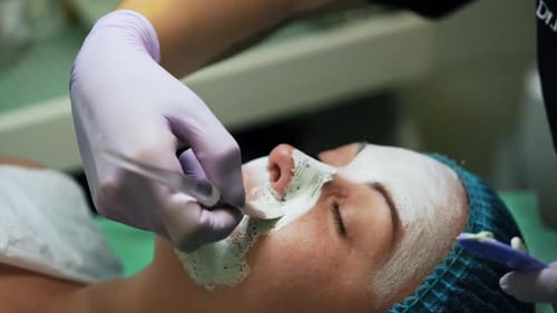 Covering Caucasian woman’s face with white mask. Cosmetology procedures at beauty salon. Close up.