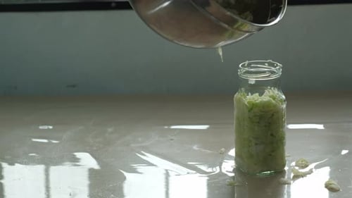 Pouring shredded cabbage juice out of stainless steel bowl into glass jar of Sauerkraut -static clos