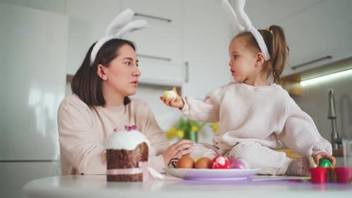 A cute daughter feeds her mother with an egg against the background of a white kitchen. Happy Easter