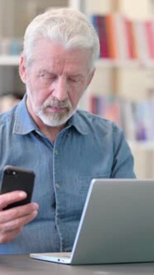 Senior Man Using Phone and Laptop Indoors