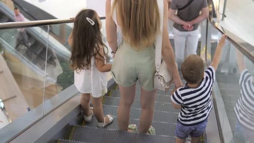 Une jeune mère et ses enfants montent sur l'escalator du centre commercial