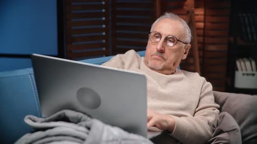 Senior Man Uses Laptop at Home on Couch