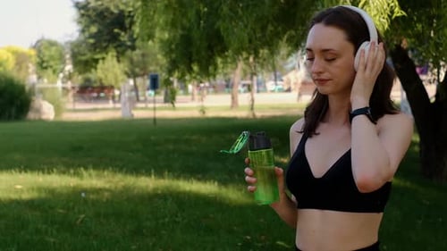 Young happy girl doing yoga in the park, listening to music with headphones, sitting in lotus positi