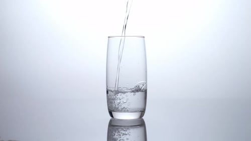 Drinking Water Being Poured Into A Glass On The Light White Screen Background In The Studio