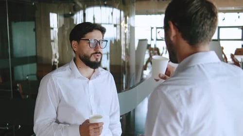Two Businessmen Engage in Conversation While Holding Coffee Cups in a Bright Office They Wear White