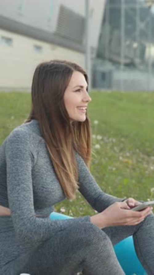 Smiling Woman Using Phone After Workout in Park