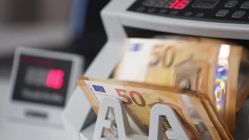 Orangefarbene Banknoten im Wert von fünfzig Euro drehen sich schnell in einer Bargeldzählmaschine.