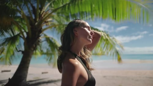 Woman Standing on Beach Next to Palm Tree