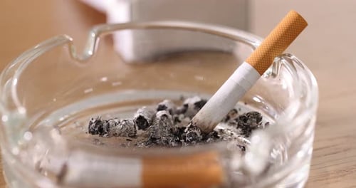 Cigarette butt smoldering in ashtray on wooden table, closeup