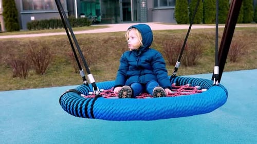 Child Enjoys Swinging on a Large Circular Swing in a Park on a Chilly Day