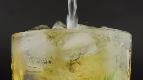 Shot of hand pouring cold tequila from a bottle with lemon and salt on black background.