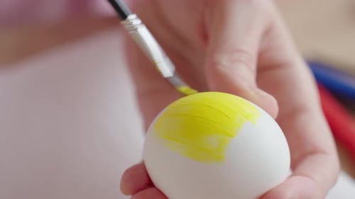 Hände bemalen Osterei mit gelber Farbe