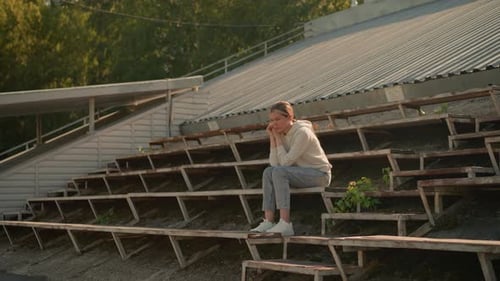 Thoughtful Woman in Casual Attire Sitting on Rustic Stadium Bleachers