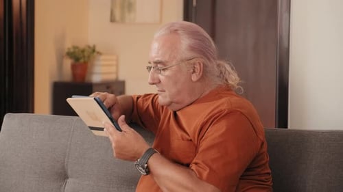 Man Using Tablet Sitting on Gray Couch Indoors