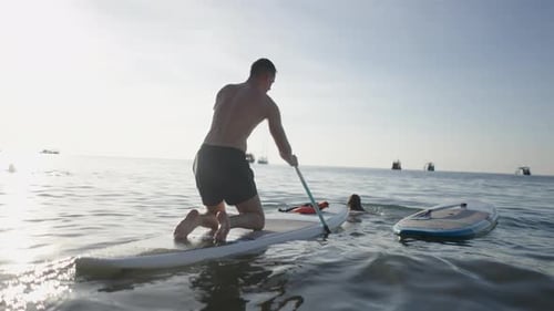 Rear Shot of a Couple Paddle Surfing in the Sea Water in Thailand