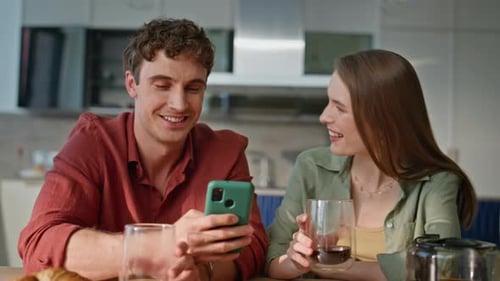 Young Couple Using Phone Together at Kitchen Table