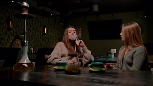 two young female friends are sitting relaxed in a hookah bar smoking hookah and having fun chatting