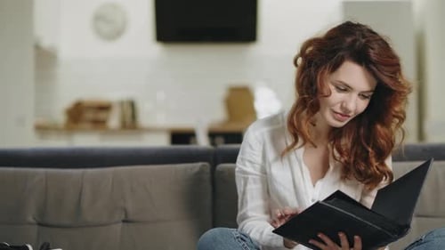 Woman Sitting on Sofa Looks Through Photo Album