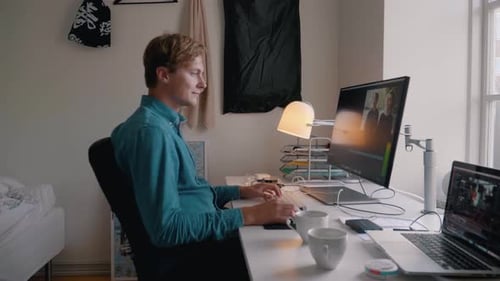 young man in a denim shirt working by the computer in the evening and rubbing his eyes