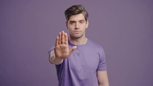Portrait Of Serious Man In Violet TShirt Showing Rejecting Gesture By Stop Palm