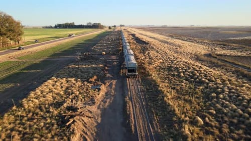 Drone aérien cinématographique au coucher du soleil capturant un vaste paysage rural grâce au transport logistique par train