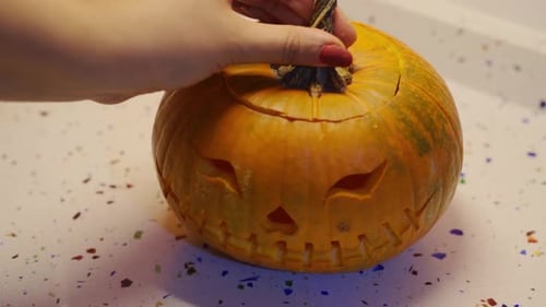 Young female hands put top on halloween pumpkin on kitchen counter