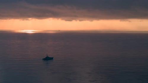 Wide aerial view of a Royal Navy Warship sailing on a calm sea at sunrise.