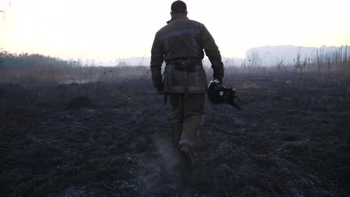 Firefighter Walks Through Burnt Field Aftermath at Sunrise