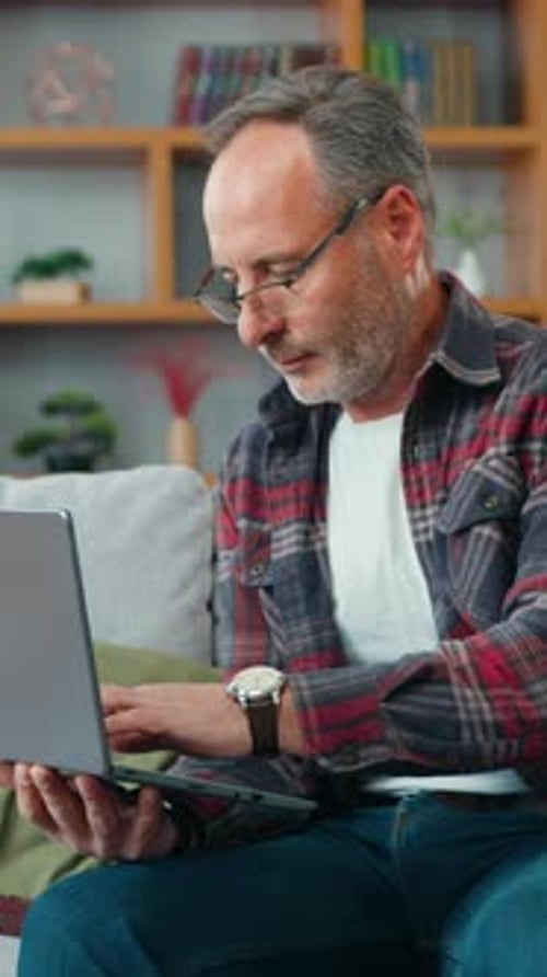 Handsome Mature Man Working on Laptop While Sitting on a Sofa in Living Room Male Learning Using