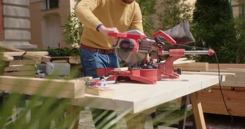 Man Cuts Wood with a Power Saw Outdoors