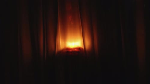 Candle Flickering in Dark Room Behind Brown Curtains