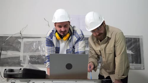 Men in Hard Hats Look at Laptop at Workplace
