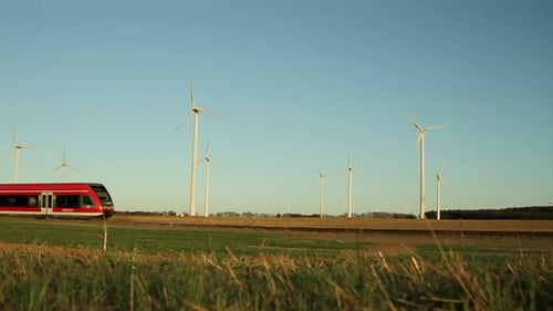 Roter Zug durchquert ländliche Landschaft mit Windturbinen vor strahlend blauem Himmel, tagsüber