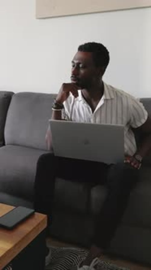 Vertikales Video: Afroamerikanisches Paar auf dem Sofa, Frau kommt an und zeigt auf den Laptop und teilt den Erfolg