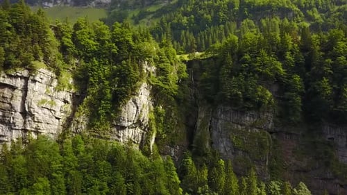 flight towards a small waterfall coming out of the cliff edge. Beautiful forest in the Swiss Alps