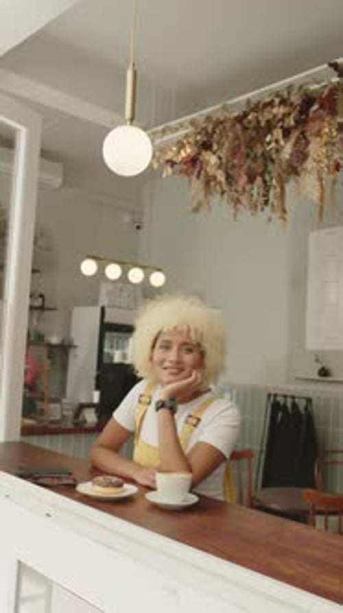 Vertical video: Woman in cafe smiling, sitting at counter with coffee and donut