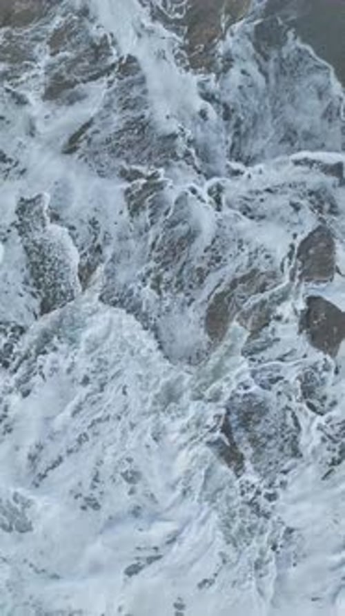 Vertical Video Aerial Perspective of the Mediterranean With Crashing Waves and Foam Flying During a