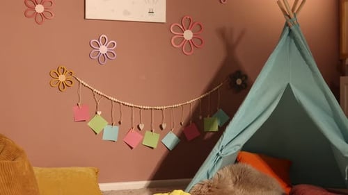 Colorful paper notes and decor hanging on brown wall near toy wigwam in stylish children's room