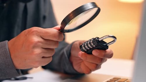 A hacker inspects a combination lock with a magnifying glass.