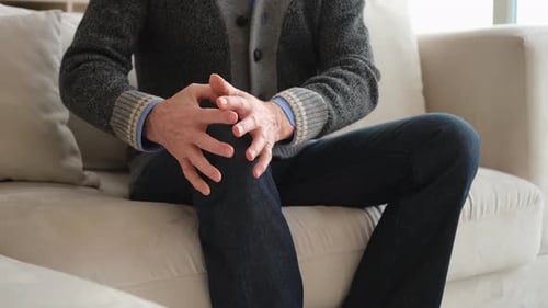 Senior Adult Rubs Knee on Couch