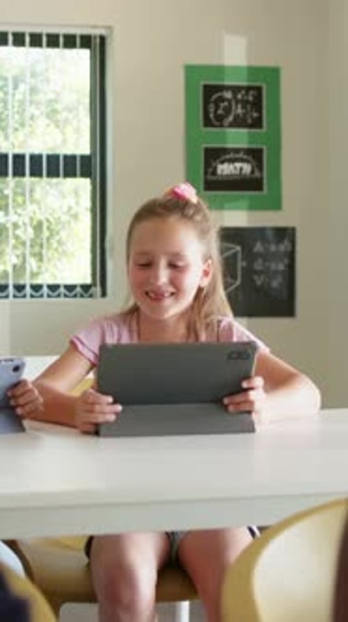 Vertical video: Entering right edge peer drawing center girl in pink holding tablet discussing math
