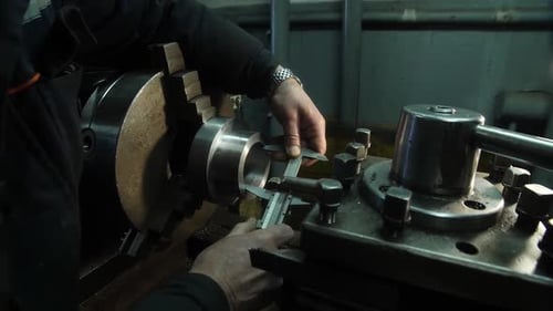 Hands of lathe operator in uniform measuring metal part with caliper
