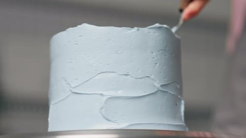Close Up Female Baker in a Professional Close Up Kitchen Distributes Blue Cream Onto Sponge Cake