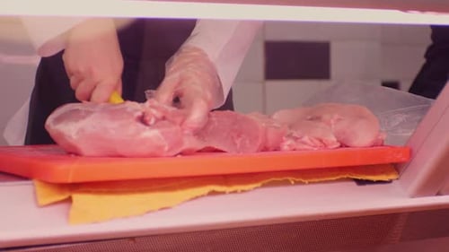 The butcher cuts pork in the shop window.