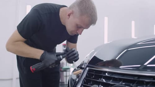 Man Polishes Black Car in Automotive Shop